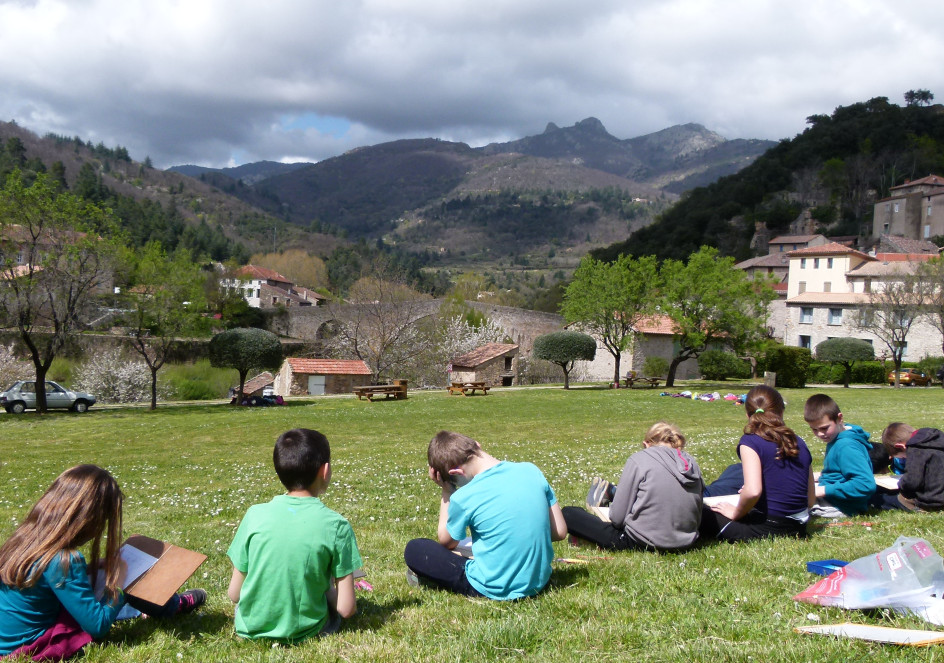 Enfants assis sur l'herbe, face à un village.